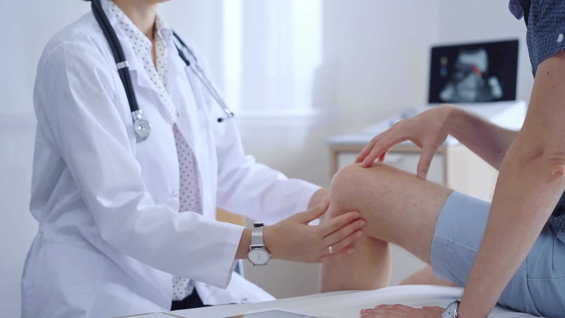 A doctor examines a patient's knee, checking for injuries.